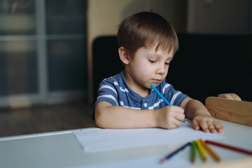 Adorable little toddler boy passionately drawing with color pencils. Image with selective focus 