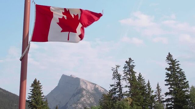 Canada flag with Rundle mountain. The wind blows the Canada flag in blue sky sunny day with beautiful scenery of Banff national park. Canada nation day concept.
