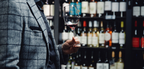 Concept choice of alcohol, hand of male sommelier in suit holds glass of red wine