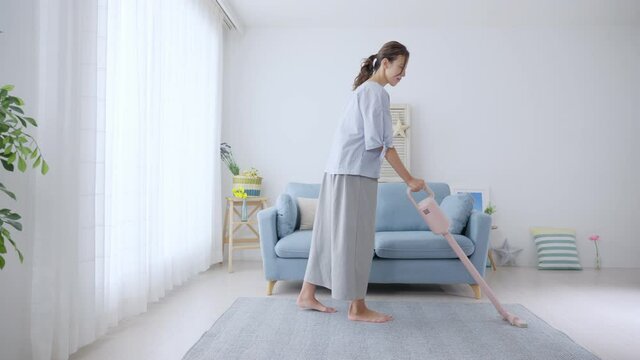 部屋の床に掃除機をかける若い女性・主婦