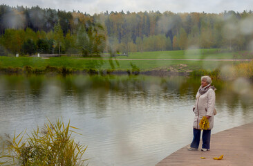 Fototapeta premium An elderly woman walks in an autumn park on a cloudy day.