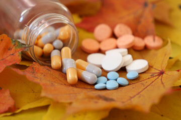 Pills on yellow and red maple leaves, bottle of capsules and scattered tablets. Concept of nutrition supplements, antidepressants, vitamins for immunity in autumn flu season