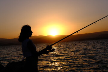 silhouette of woman fishing at sunset.