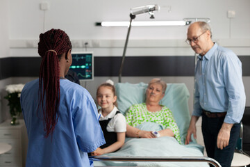 Obraz premium African american asisstant analyzing medical expertise explaining sickness treatment to elderly sick woman. Caring family checkup retired patient to support her during clincal therapy in hospital ward
