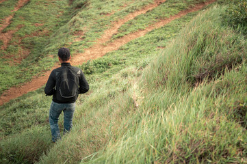 Naklejka na ściany i meble Backpacker man walking in the countryside, adventurous man descending from a hill, man with backpack going down a hill