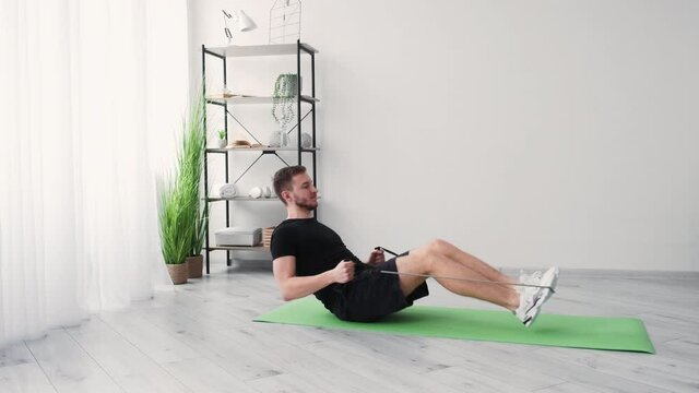Expander workout. Sportive man. Home training. Fitness gym. Healthy lifestyle. Smiling guy doing exercise with resistance band in light room interior copy space.