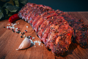 BBQ with homemade pork ribs, garnished with herbs, coarse salt, pepper, garlic and onions. Barbecue still life. Focus on the foreground.