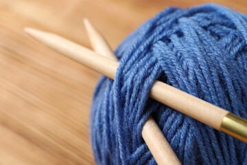 Blue ball of yarn with knitting needles on a light wooden table