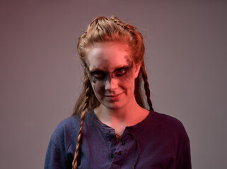 Closeup portrait of young red haired woman with black barbarian facepaint wearing medieval viking inspired costume Holding  sheep skull for ritual  posing against studio background with red lighting