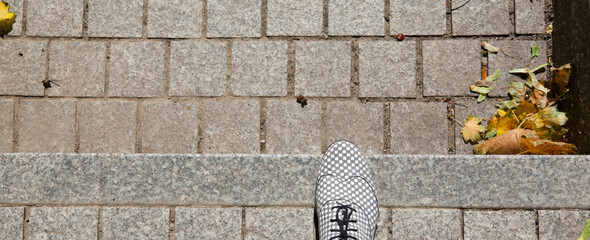 Fragment of a white and gray shoe with a geometric pattern on a cobblestone staircase with lying yellowed leaves, top view.