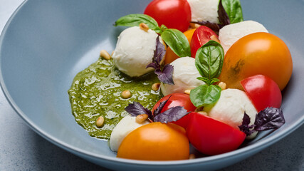 Close up italian caprese salad with ripe tomatoes, pesto, nuts, basil and mozzarella cheese in grey deep plate. Selective focus