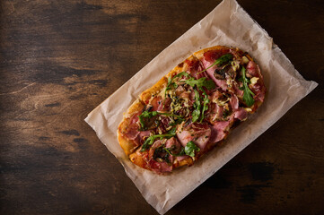Rectangular Roman pizza with prosciutto ham, tomatoes, mozzarella, mushrooms and arugula on wooden...