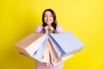 Photo of cute millennial lady hug bags like shopping wear sweater isolated on yellow color background