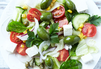Healthy Salad with Feta Cheese, Green Olives, Baby Spinach, Cucumber, Cherry Tomatoes and Capers. Bright wooden background. Top view. Close up. 