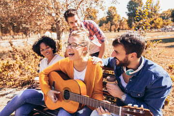 Group of young people hangout in the park.They sitting on bench ,singing and playing guitar.