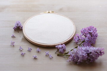 Fototapeta na wymiar Flat lay top view photo of a mockup with embroidery hoop and llilac flowers.