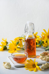 Jerusalem artichoke topinambour syrup in bowl and bottle on white background. Vertical format. Sugar substitute for raw vegan desserts.