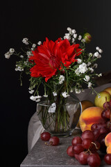 Still life with a red flower and fruit on a dark background