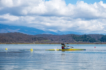 Adler, Russia - March 27, 2021 male athlete quickly floats on a long boat rowing oars. background mountain landscape
