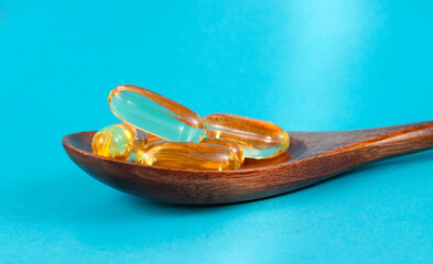 Fish oil or omega capsules on a wooden spoon on a blue background.