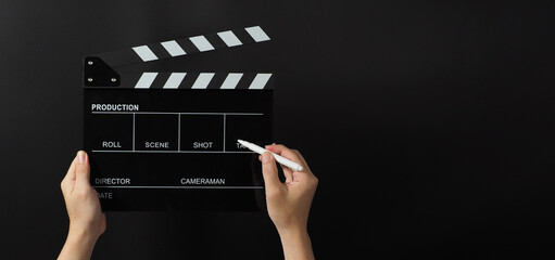 Hand is holding black clapper board or movie slate and marker Pen on black background