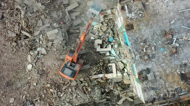 A demolition excavator destroys an old unusable building. Destruction of walls and concrete blocks.  Drone view.