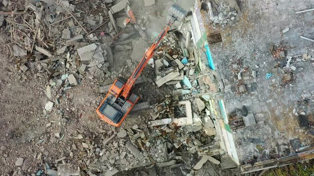 A demolition excavator destroys an old unusable building. Destruction of walls and concrete blocks.  Drone view.