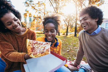 Mixed family having fun while picnicking in the park eating pizza.