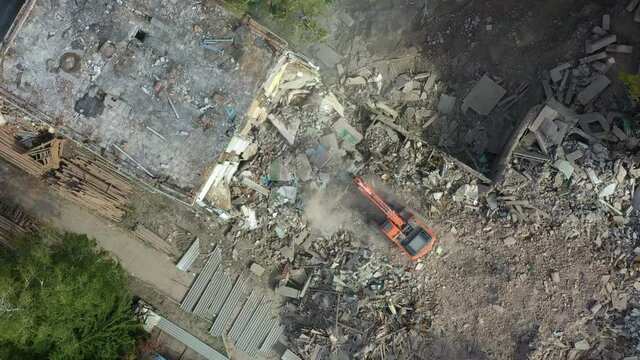 A demolition excavator destroys an old unusable building. Destruction of walls and concrete blocks.  Drone view.