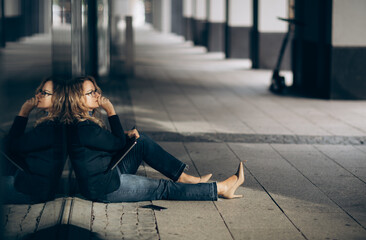 A sad business woman sits desperate on the floor with her laptop on knees, bad news.