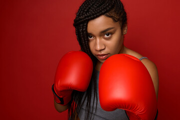 Close-up portrait of concentrated young African sports woman boxer wearing red boxing gloves,...
