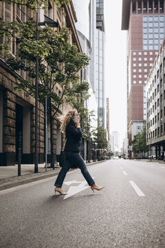 Business woman with big bag and smartphone in hand crosses the street in big city. High quality photo