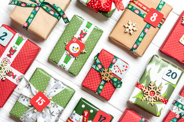 Fototapeta na wymiar Handmade wrapped red, green gift boxes decorated with ribbons, snowflakes and numbers, Christmas decorations and decor on white table Xmas advent calendar concept Top view Flat lay Holiday card