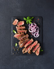 Rare beef slices on a stone board with onions and basil. Beef steak medium rare on black background.