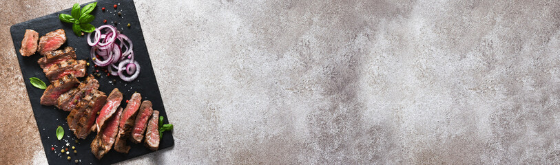 Rare beef slices on a stone board with onions and basil. Beef steak medium rare on black background.