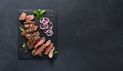 Rare beef slices on a stone board with onions and basil. Beef steak medium rare on black background.