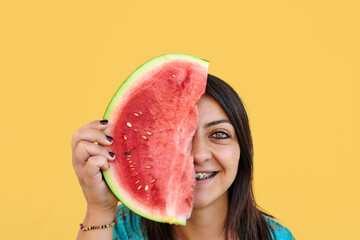 Young dark hair woman with brackes and a piece of watermelon on yellow background