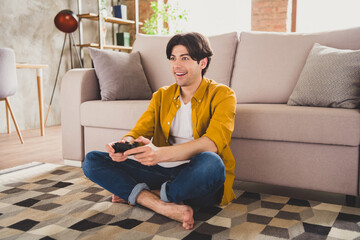 Photo of addicted player guy hold joystick gamepad play video game sit floor wear yellow shirt home indoors © deagreez