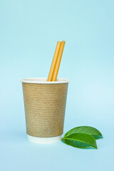 disposable eco friendly paper cup, bamboo straws and green leaves on blue background