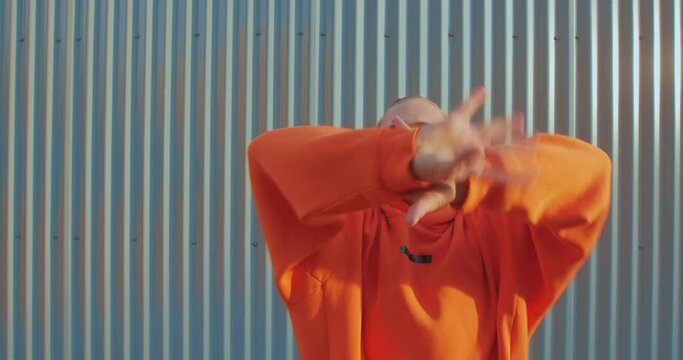 Stylish dancing lgbt guy in hoodie performing graceful contemporary dance on fence background outdoor. Gender identity