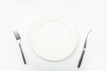 White plate with fork and knife for cutting meat pieces on white background isolated, with copy space.