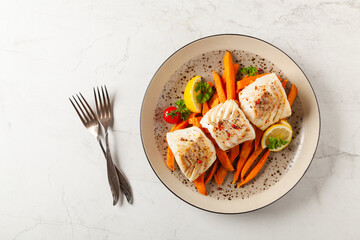 Fried pieces of cod loin, served with sweet potato fries. Light stone background.