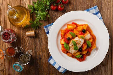 Traditionally prepared cod in Spanish. Served in tomato sauce with boiled potatoes, olivki and basil. Top view.