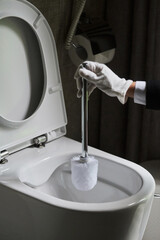 Housekeeper in a neat white apron standing scrubbing out a toilet with a brush.