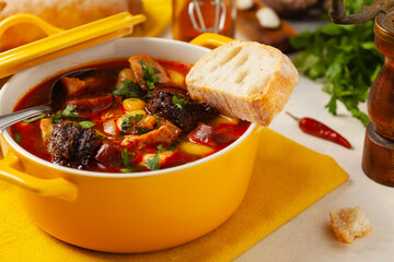 Traditional Spanish goulash soup. Fabada Asturiana. Served with a yellow clay pot with lid. Front...