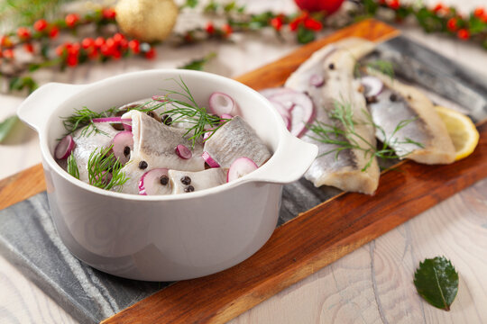 Herring fillets in oil. Served with onion in a bowl. Wooden background.