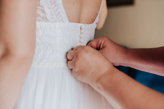 Manos de madre vistiendo de novia a su hija. Manos abotonando vestido de novia. 