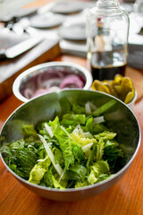 Demonstration of ingredients for cooking in the kitchen on the table. Washed roman salad in a bowl, mixed with celery. Other ingredients and jars in the background.