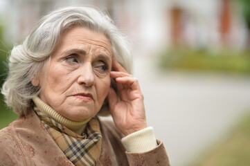 sad  senior woman with headache  in  park