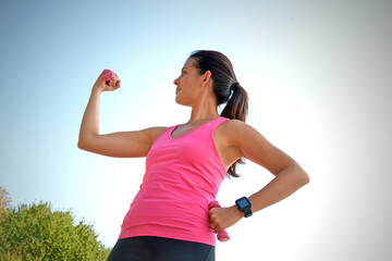Naklejka premium Outdoors young latin woman stretching and looking her biceps arm on blue sky background.